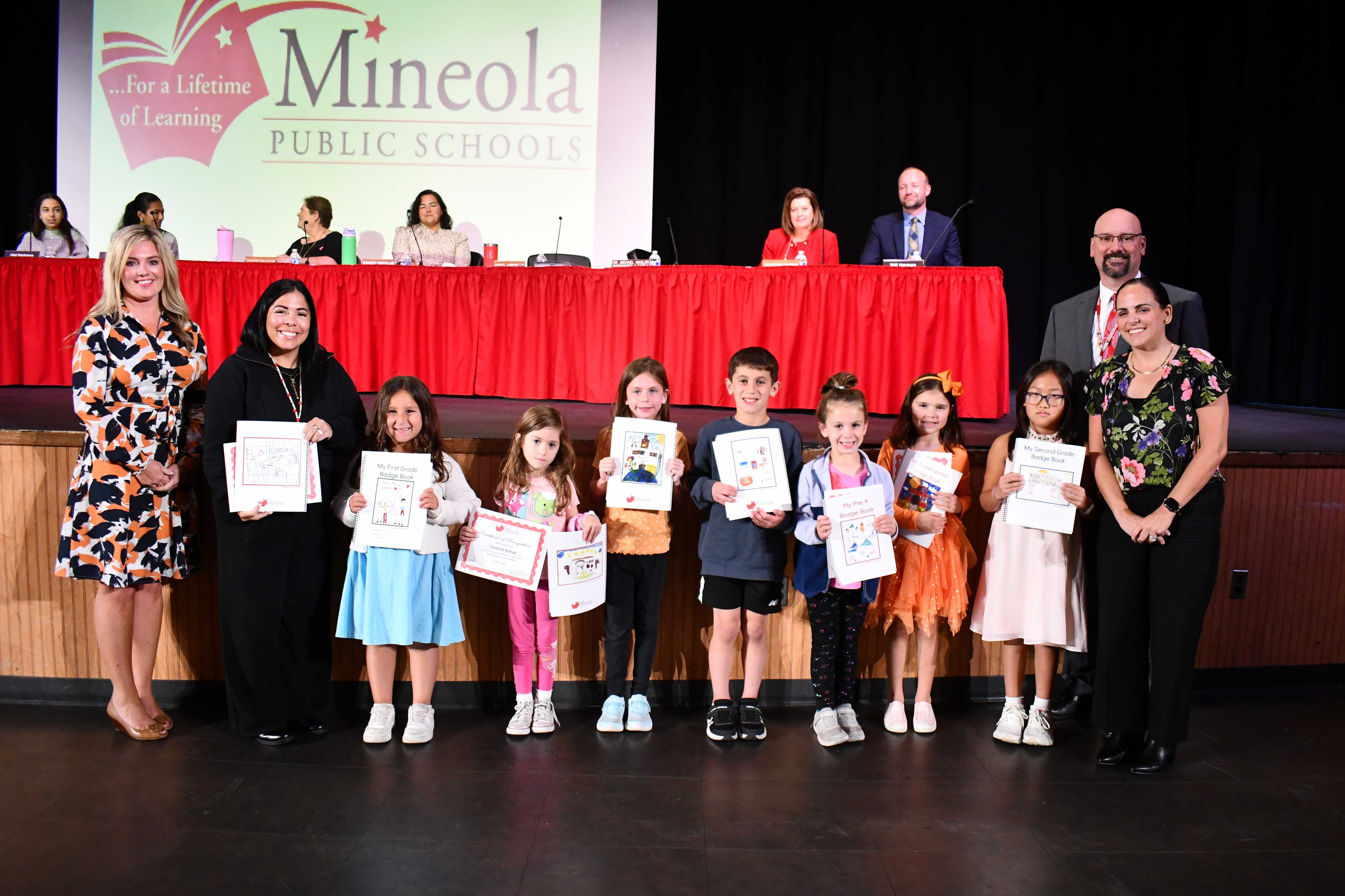 Young students holding certificates and smiling with administrators and board of education members